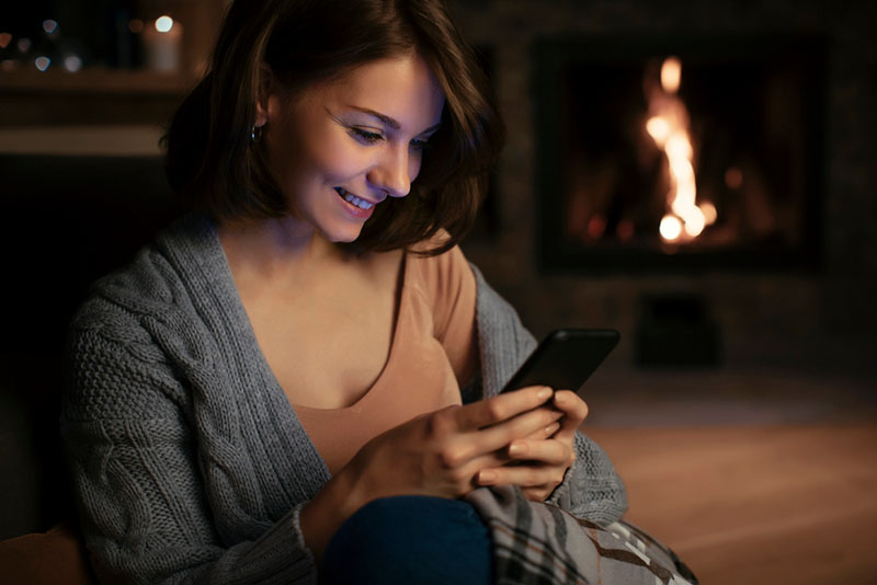 Woman using phone in front of fireplace