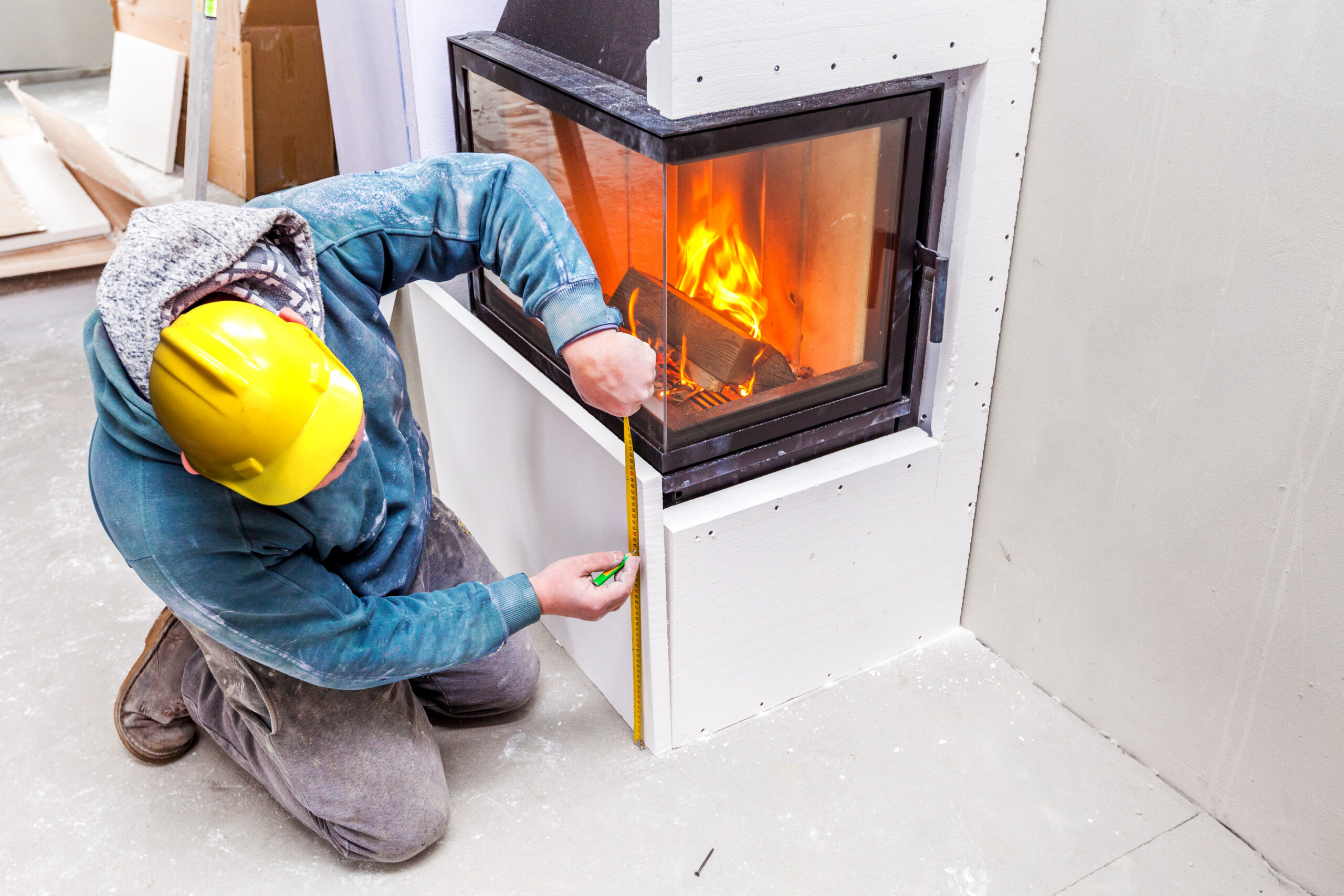 Adobe Stock image of a man installing a fireplace and taking some measurements.